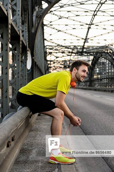 Junger männlicher Läufer auf der Brücke ruhend