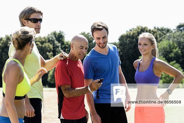 Reife männliche Trainerin und eine Gruppe erwachsener Läufer  die auf die Stoppuhr schauen.
