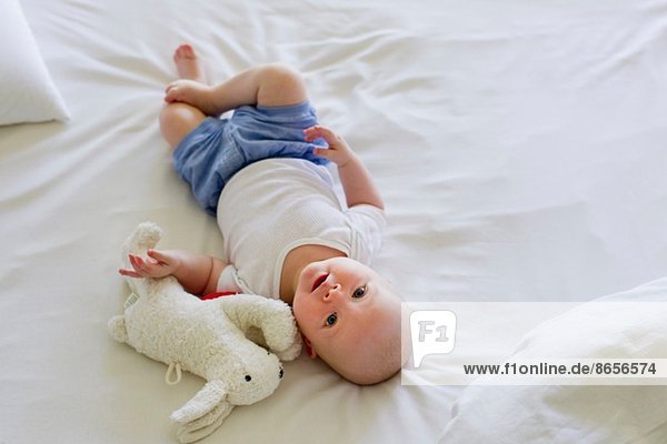 Baby girl lying on bedclothes with soft toy