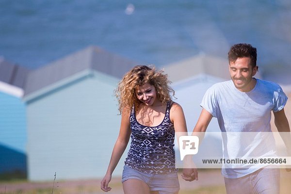 Junges Paar hält sich an den Händen mit Strandhütten im Hintergrund