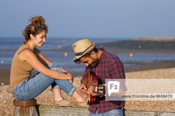 Junges Paar am Strand  Mann spielt Gitarre
