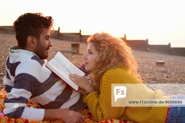 Young couple lying on beach  woman reading book