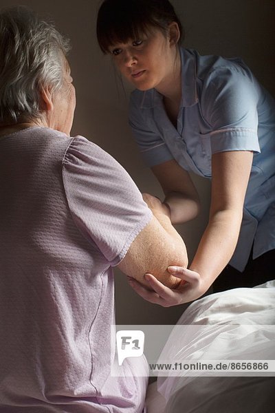 Körperpflege-Assistentin hilft Seniorin aufzustehen