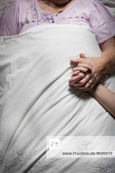 Abgeschnittene Bilder einer jungen Frau  die die Hand einer schlafenden älteren Frau hält.
