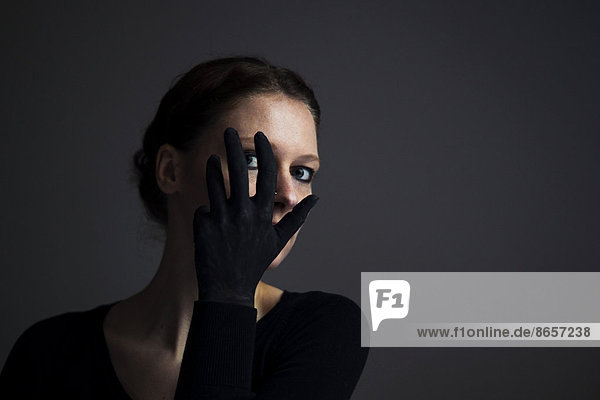 Woman holding her hand with a black glove in front of her face