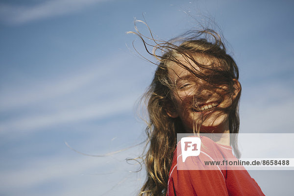 Ein lächelndes neunjähriges Mädchen  dem der Wind die Haare übers Gesicht weht.
