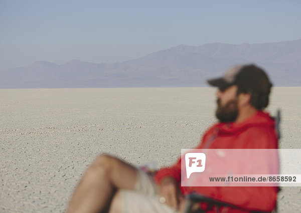 Mann sitzt auf einem Stuhl in der weiten  kargen Wüste  verschwommener Fokus