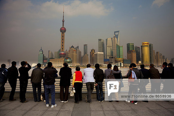 Eine Reihe von Menschen  die auf die Skyline von Shanghai Pudong blicken  darunter der Oriental Pearl Tower  das Shanghai World Financial Center und der Jin-Mao-Tower  von der Seite des Huangpu-Flusses aus