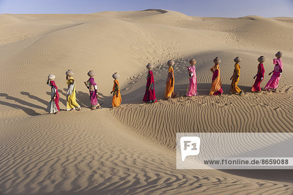 Frauen tragen die Verantwortung dafür  Wasser aus den spärlichen Brunnen in Rajasthans riesiger Thar-Wüste zu holen. Beim Trekking am Rand einer Sanddüne balancieren die Frauen gekonnt große Wassergefäße aus Ton auf ihrem Kopf. Rajasthan  Indien