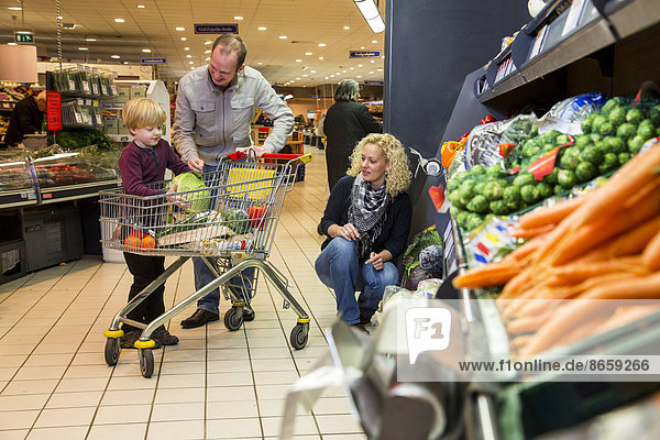 Familie mit Einkaufswagen beim Einkaufen im Supermarkt  Gemüseabteilung  Deutschland