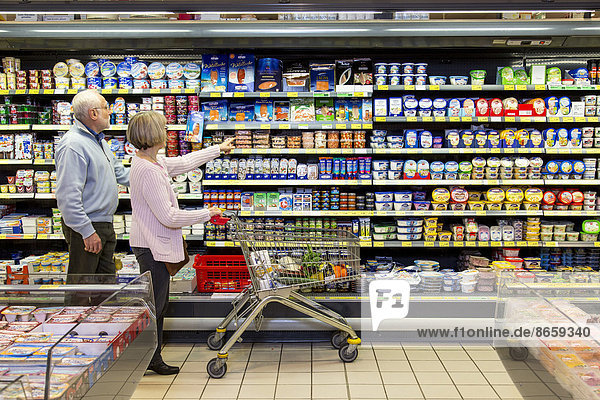 Senior couple shopping with a shopping trolley in the refrigerated dairy section in a supermarket  Germany