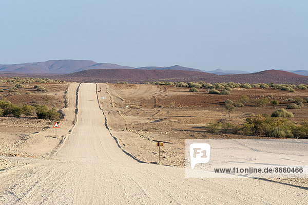 Breite gerade Schotterstraße in trockener Landschaft Region Kunene Namibia