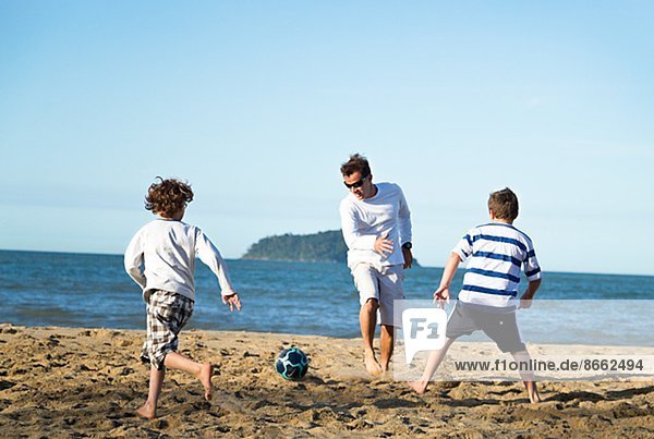 Boys with father playing soccer on beach