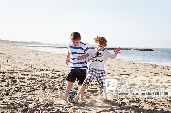 Two boys playing soccer on beach