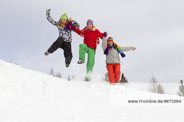 Drei junge Erwachsene in bunter Winterkleidung springen im Schnee  Kärnten  Österreich