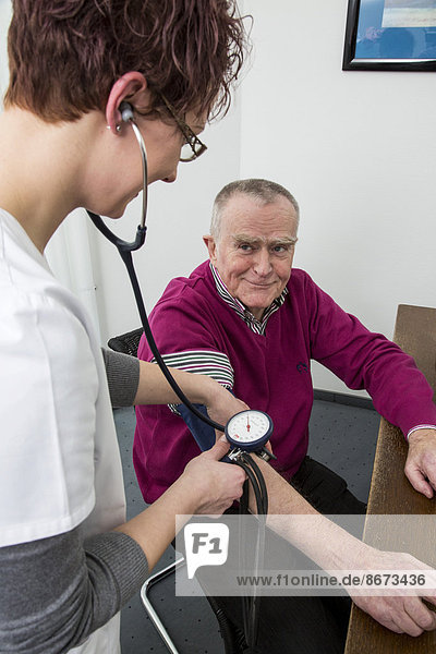 Arztpraxis  älterer Patient bekommt von einer Arzthelferin den Blutdruck gemessen  Deutschland