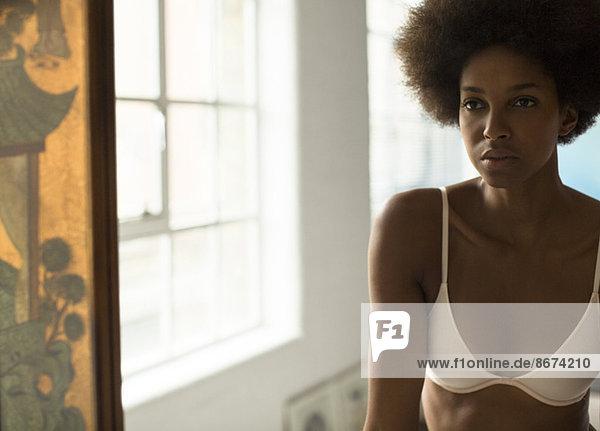 Serious woman in bra standing at mirror