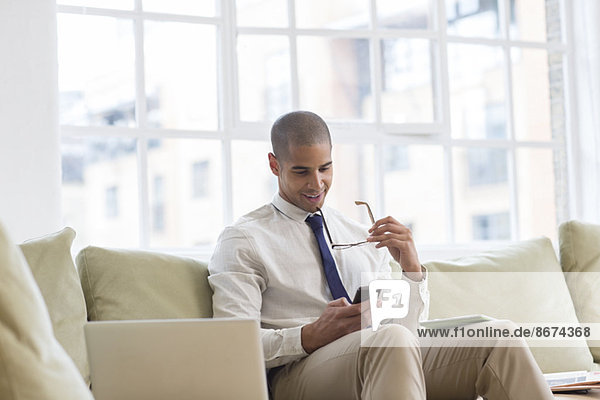 Businessman using cell phone on sofa