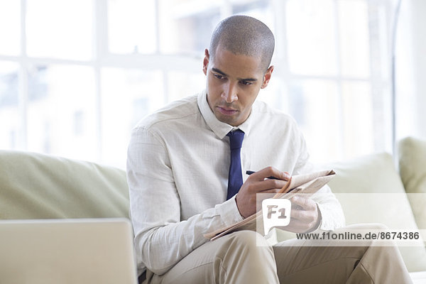 Businessman making notes from laptop on sofa