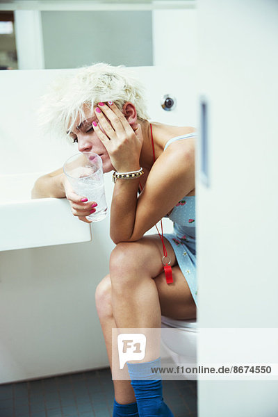 Hungover woman sitting on toilet in bathroom