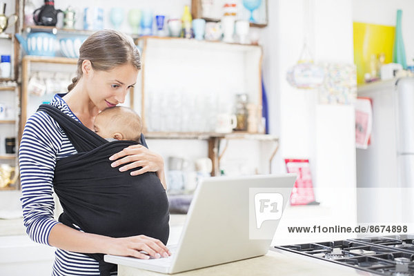 Mother with baby boy using laptop in kitchen