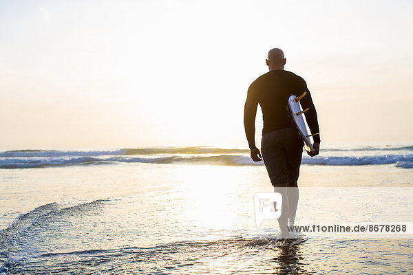 Mixed race man walking with surfboard on beach