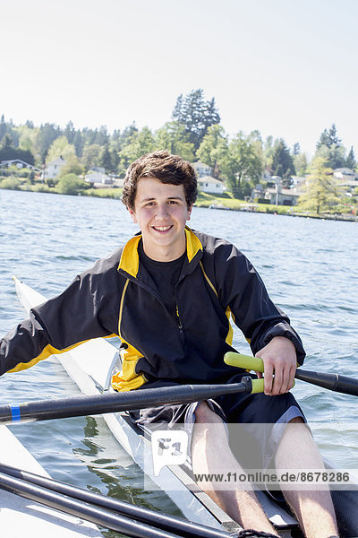 Mixed race teenage boy rowing scull on lake