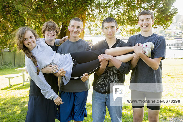 Caucasian teenage boys holding girl in park