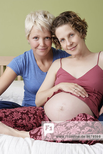 Caucasian Pregnant Lesbian Couple Relaxing On Bed