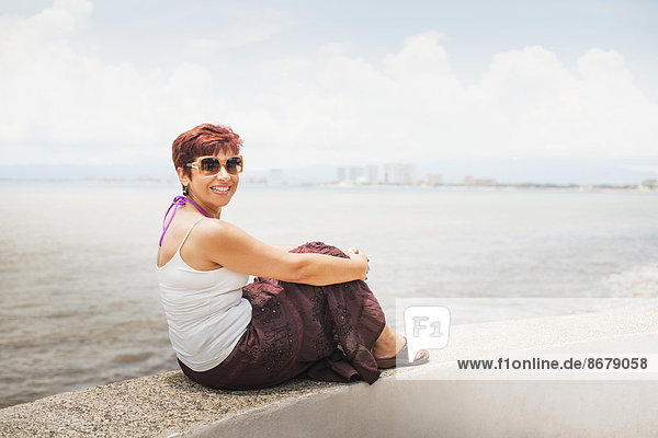 Hispanic woman sitting on stone wall overlooking beach