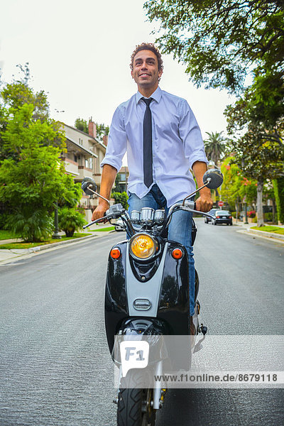 Hispanic businessman standing on scooter on neighborhood road