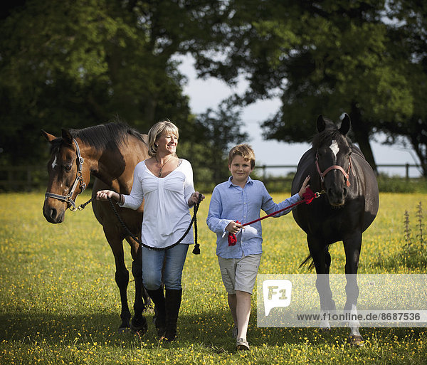 Eine Frau und ein Junge gehen mit zwei Pferden auf einem Feld spazieren.