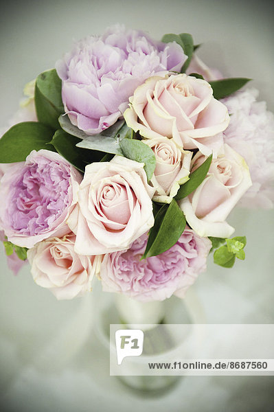 Ein Brautstrauß aus pastellfarbenen rosafarbenen Rosen und blassen Lavendelpfingstrosen mit kleinen grünen Blättern.