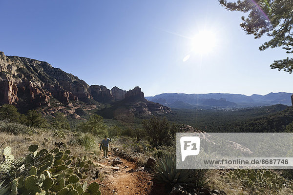 A woman in a sunhat walking up a trail in the Sedona national park  hiking in the midday sun. Mountain landscape.
