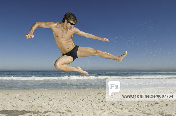 Ein junger Mann macht am Strand von Kapstadt einen Sprung im Karatestil.