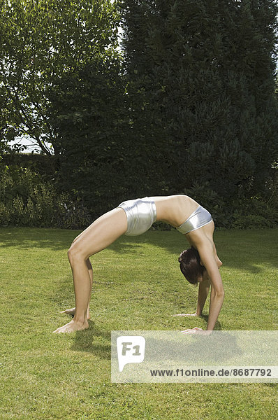 Eine junge Frau zeigt ihre Beweglichkeit  lehnt sich in einem Bogen nach hinten  Hände und Füße auf Gras