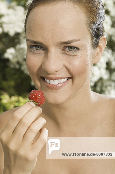 Eine junge Frau hält eine Erdbeere in der Hand.