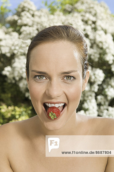 Eine junge Frau hält eine Erdbeere zwischen ihren Zähnen.