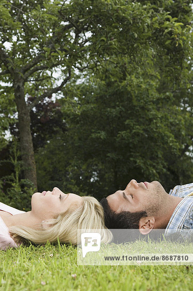 Ein Paar auf dem Rücken liegend  den Kopf auf dem Gras berührend