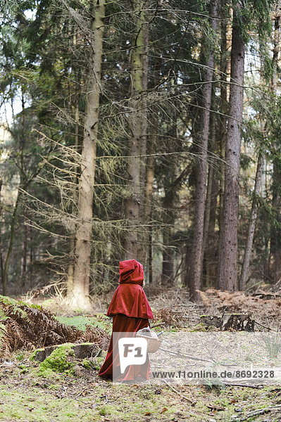 Kleines Mädchen verkleidet als Rotkäppchen im Wald stehend