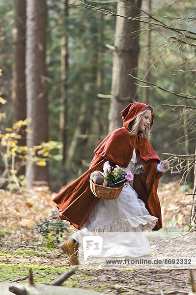Girl masquerade as Red Riding Hood riunning in the wood
