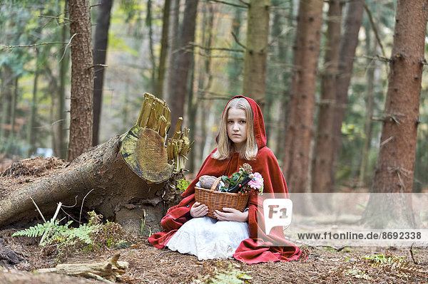 Girl masquerade as Red Riding Hood sitting on the ground in the wood