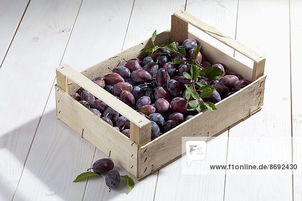 Wooden box with plums on wooden table
