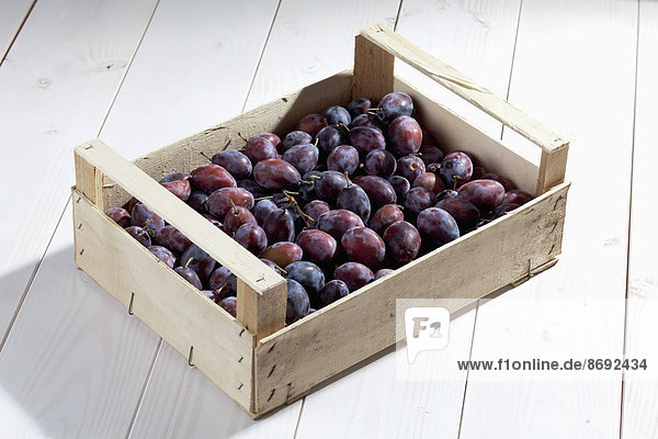 Wooden box with plums on wooden table