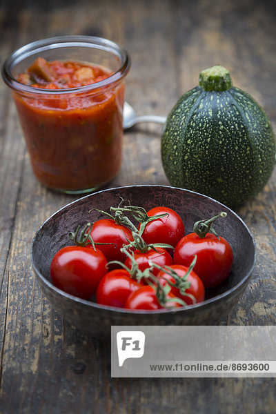 Metallschale mit Kirschtomaten  Einmachglas mit Tomatensauce und Zucchini auf Holztisch