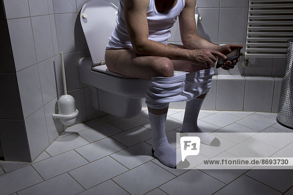 Germany  Man sitting on toilet  using smart phone