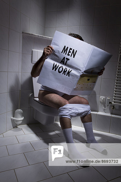 Germany  Man sitting on toilet  reading newspaper