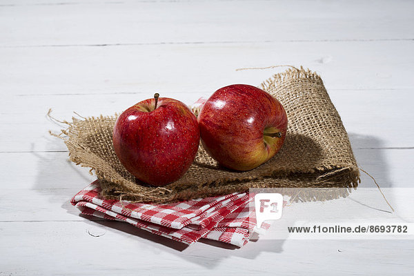 Zwei rote Äpfel auf Jute  Stoffserviette und Holztisch