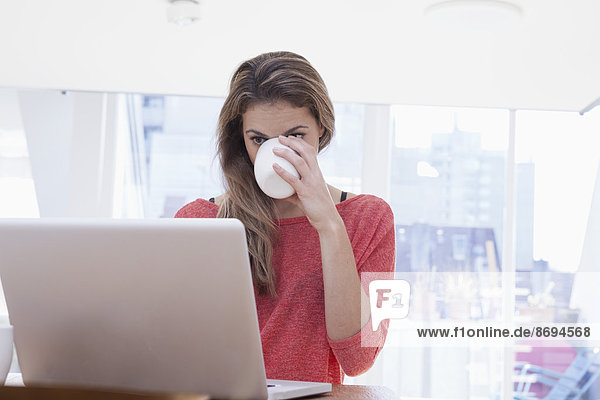Frau trinkt Kaffee während der Benutzung des Laptops