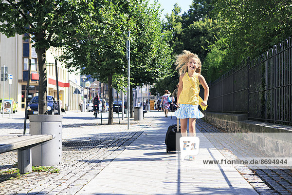 Girl with pulling suitcase running on sidewalk